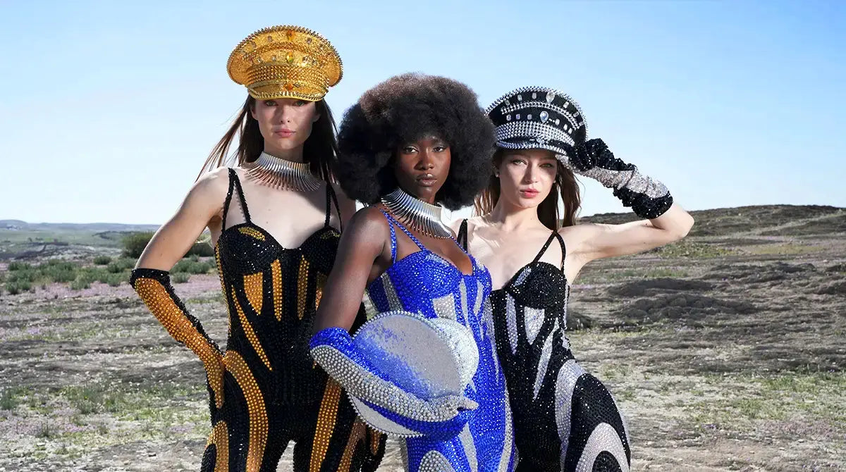 Three women in avant-garde fashion posing outdoors with a clear blue sky.