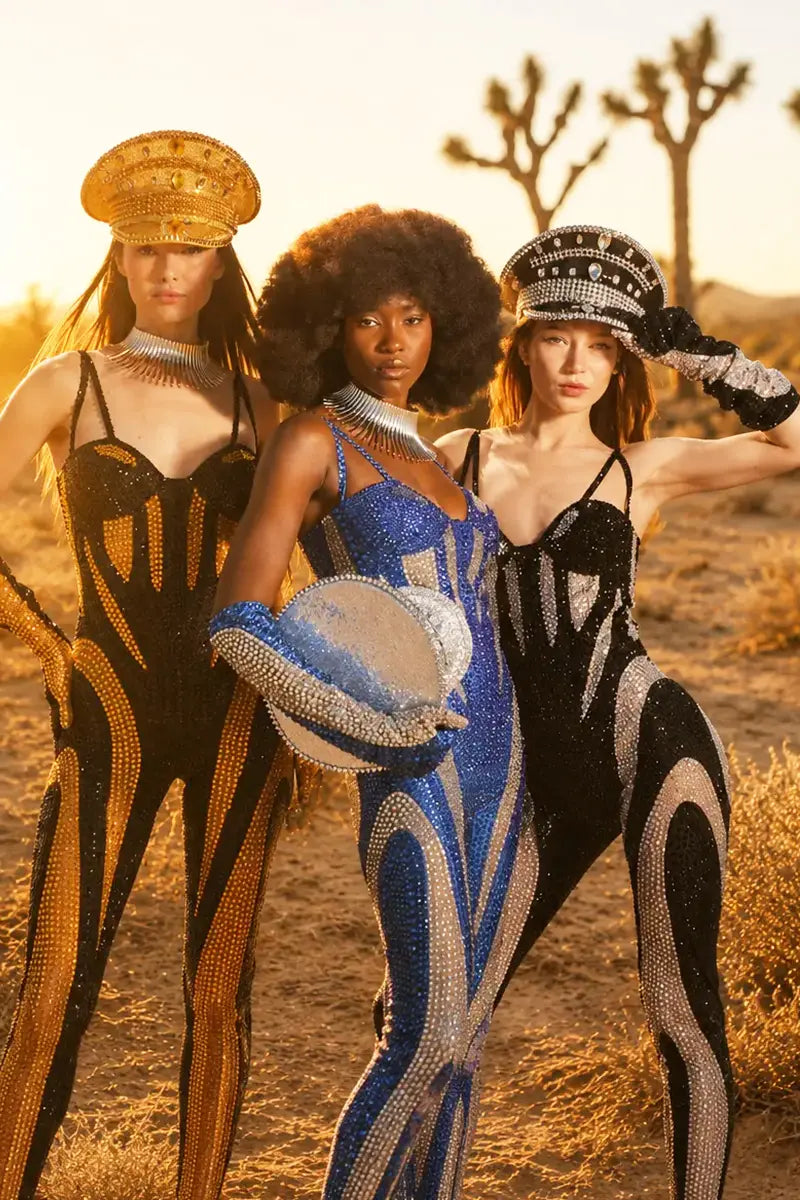 Three women in futuristic outfits standing in a desert landscape with cacti.